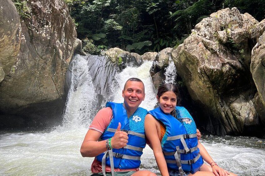 Two people in blue life vests sitting by a waterfall. 1