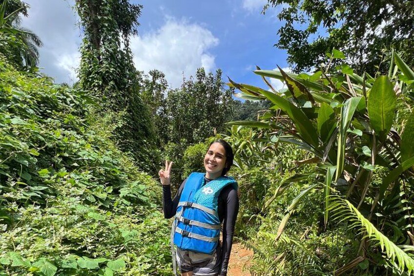 Una persona con chaleco azul de pie sobre un sendero rodeado de abundante follaje verde. 5