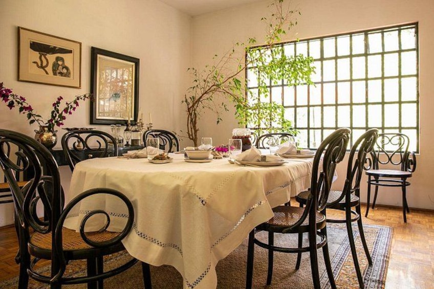 A dining room with a table set for four, surrounded by black chairs, with a window and a plant in the background. 2