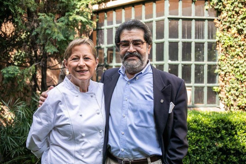Dos personas de pie frente a un edificio con amplios ventanales y vegetación. 4