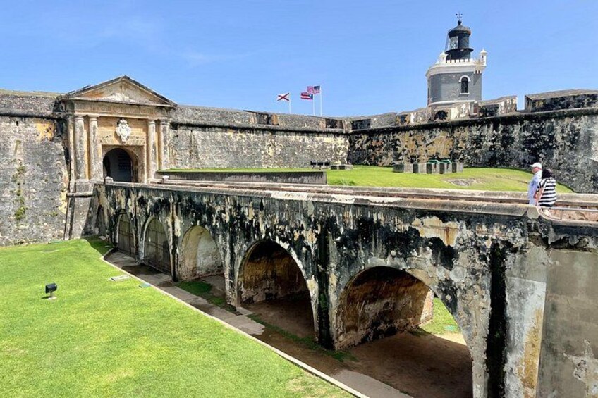 A historic stone bridge with arches, a grassy area, and a building with a tower in the background. 5