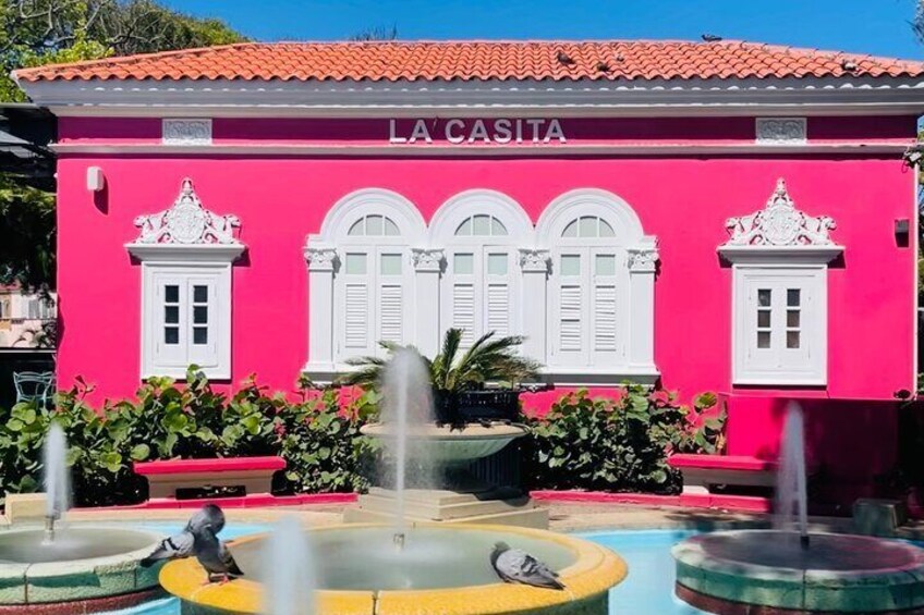 Un bâtiment rose appelé « LA CASITA », avec des volets blancs et une fontaine devant. 4