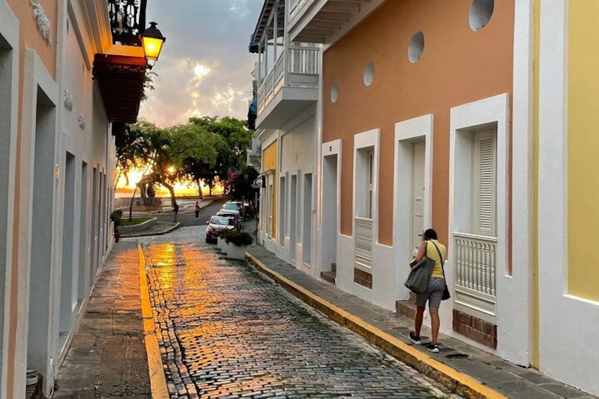 A cobblestone street with buildings, a person walking, and a sunset in the background. 2