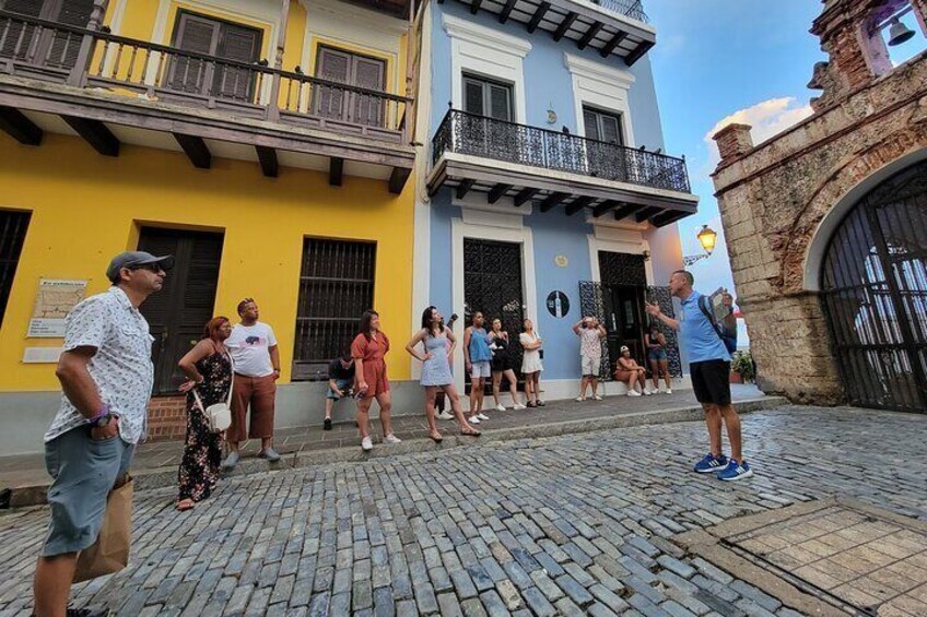 A cobblestone street with tourists and a man giving a tour. 3