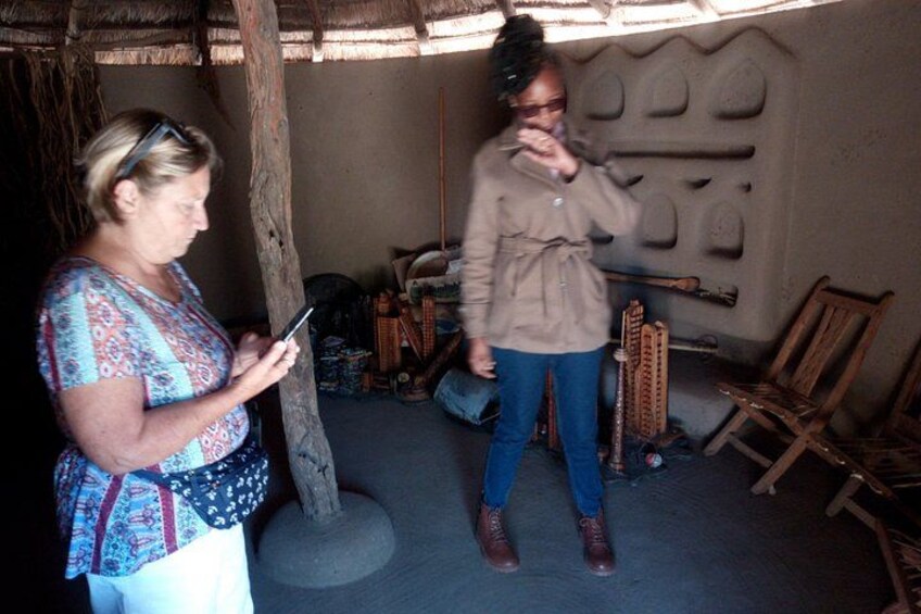 Two people in a rustic setting with a thatched roof, wooden furniture, and traditional decor. 1
