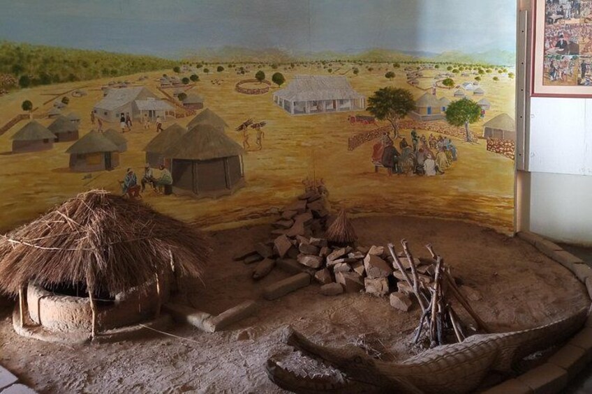 A mural of a rural village with thatched-roof huts, a central gathering area, and a landscape with trees and distant buildings. 4