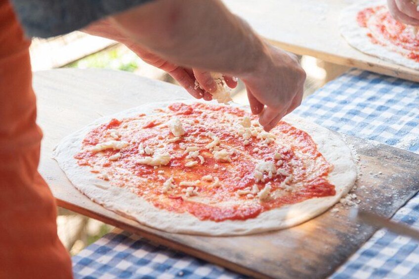 A person preparing pizza dough with tomato sauce and cheese on a wooden board. 2
