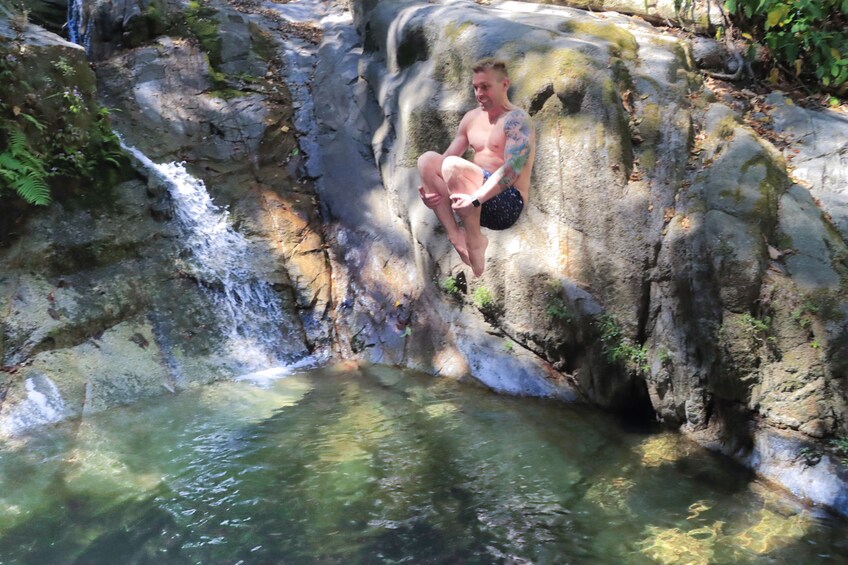 Una persona sentada sobre una roca cerca de una cascada en un área boscosa. 1