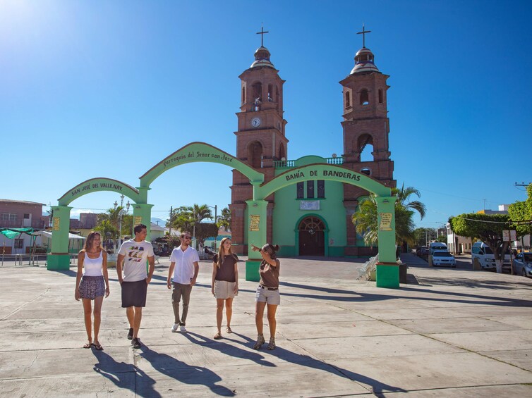 A group of people standing in front of a church with two towers and a green archway. 1