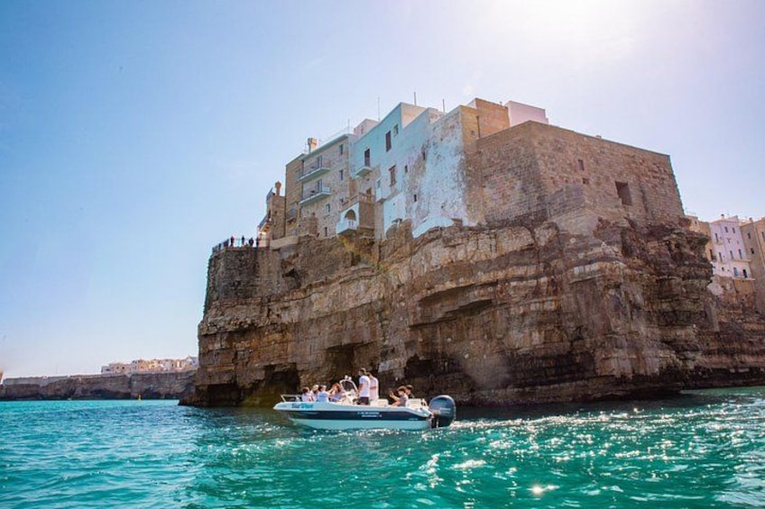 A boat with people on a rocky coastline with buildings on top. 1