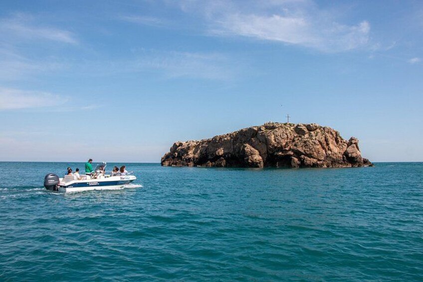 A boat with people on a clear day near a rocky island with a cross on top. 2