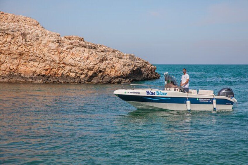 A boat named 'Blue Wave' on calm sea water with a rocky cliff in the background. 2