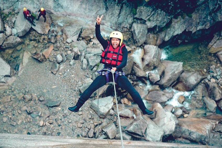 A person bungee jumping with a helmet and life jacket, surrounded by rocky terrain and a river. 2
