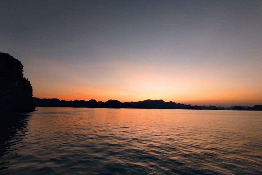 Un coucher de soleil sur une étendue d’eau calme, avec des silhouettes de terre en arrière-plan. 2