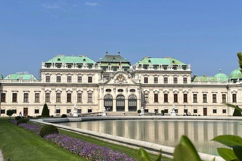A large, ornate building with a symmetrical facade, a central entrance, and a reflective water feature in front. 1
