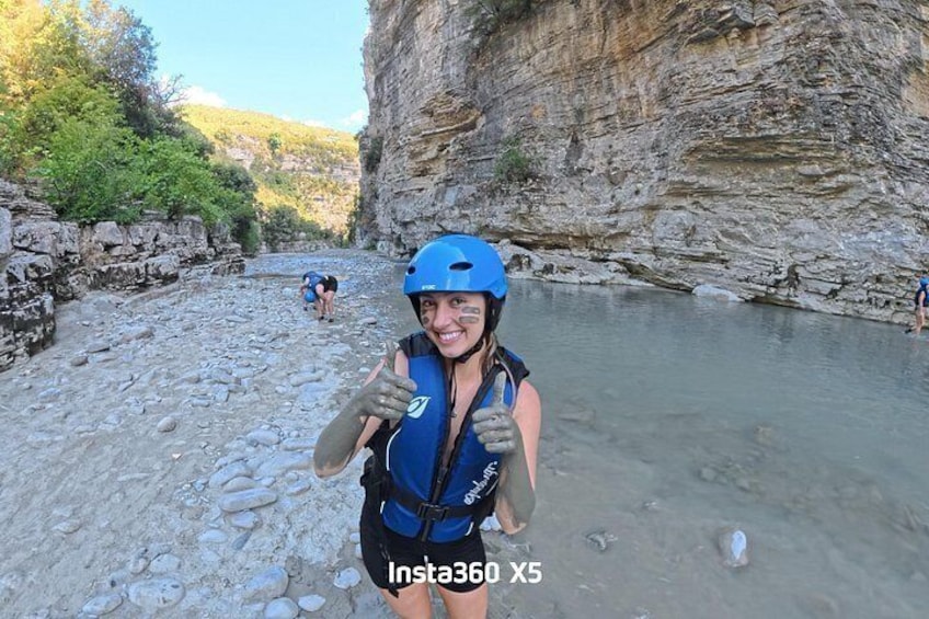 Una persona con casco azul y chaleco salvavidas de pie en la orilla rocosa de un río. 1