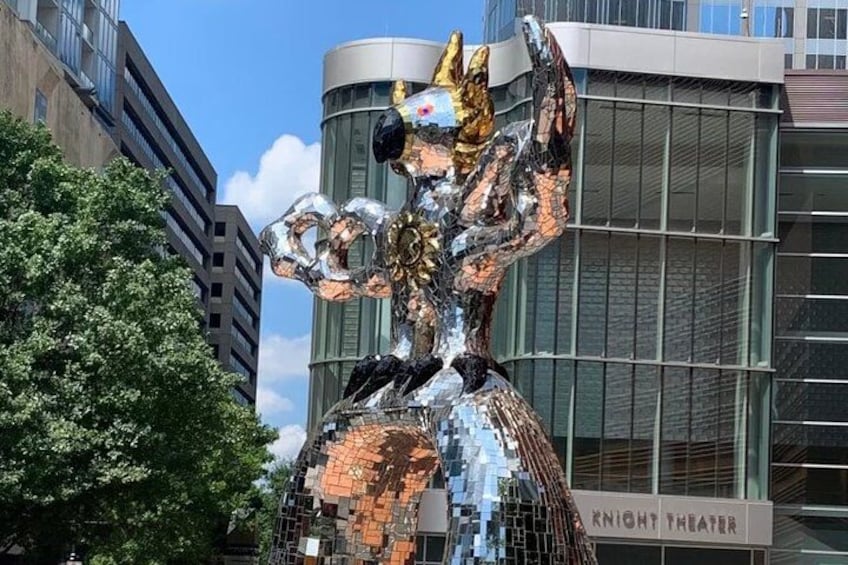 Una scultura in metallo raffigura una figura con le braccia alzate, posta di fronte a un edificio moderno con facciata in vetro. 5