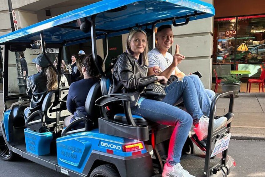 Un carrello da golf blu con passeggeri, parcheggiato in strada con un ristorante sullo sfondo. 2