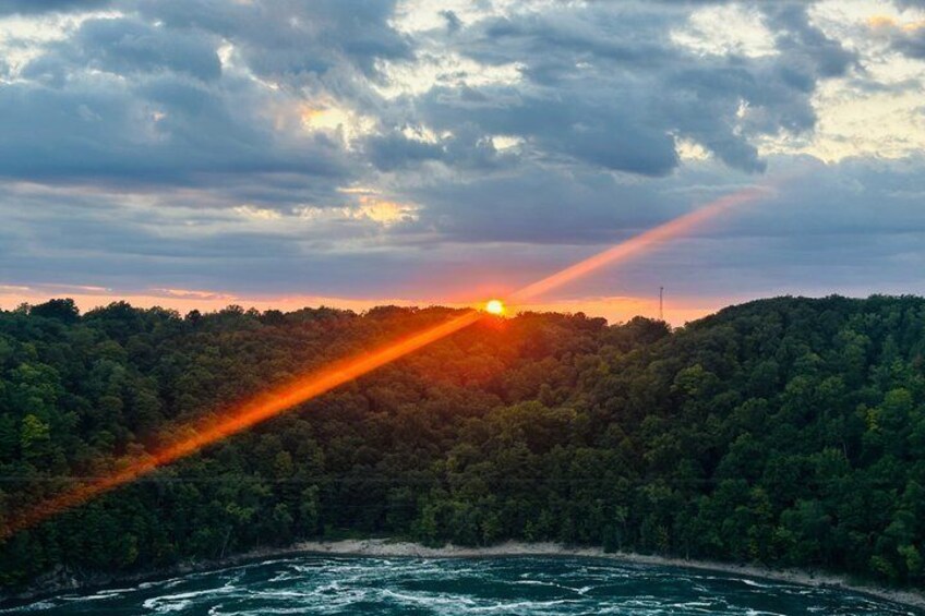 A sunset over a forested hill with a river in the foreground. 5
