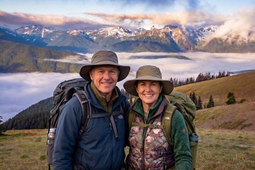 Two people hiking in a mountainous area with snow-capped peaks in the background. 1