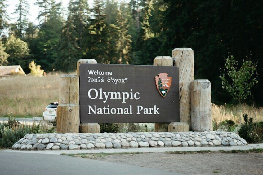 A welcome sign for Olympic National Park with a logo and a stone wall. 3