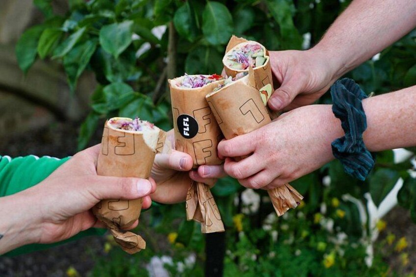 Drie mensen houden papirishoeden met eten vast, buiten met begroeiing op de achtergrond. 3