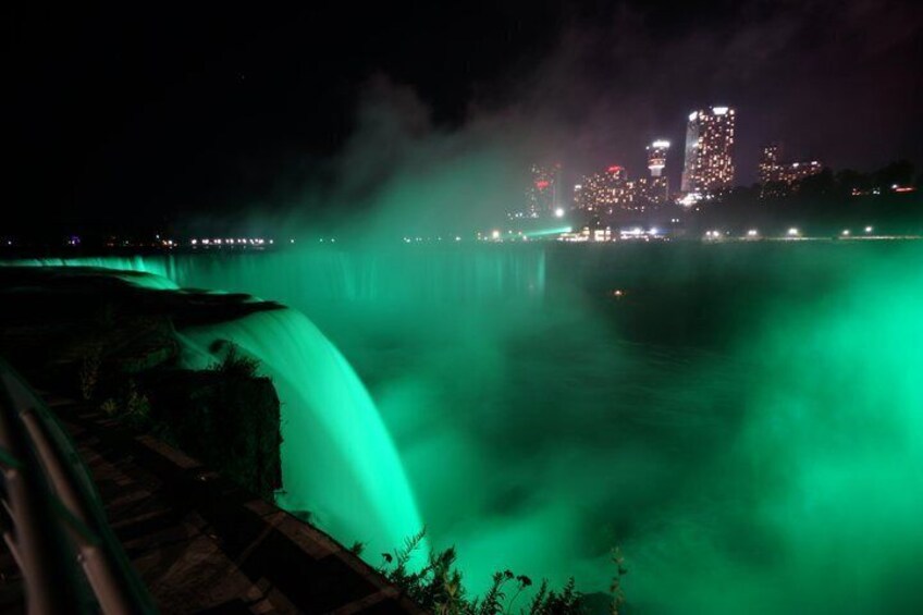 A waterfall illuminated by green lights at night with a city skyline in the background. 5