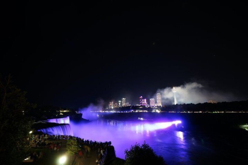 A nighttime cityscape with illuminated buildings and a waterfall. 4