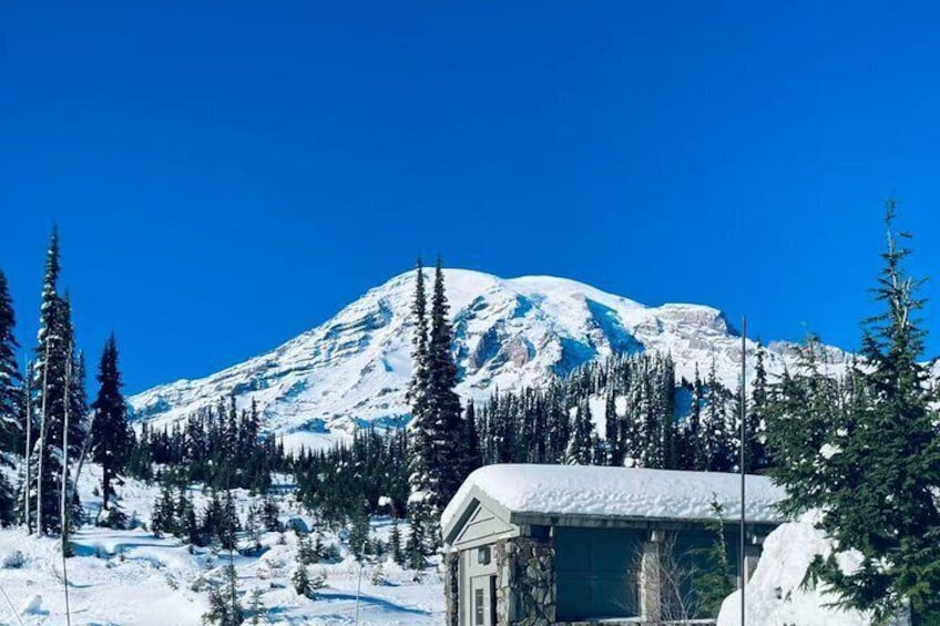 A snow-covered mountain with a clear blue sky, a small cabin, and evergreen trees. 2