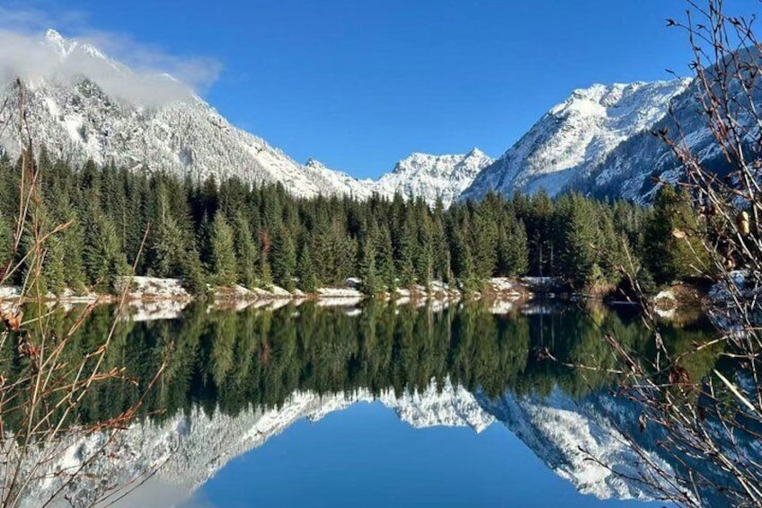 A snow-covered mountain range, a calm lake reflecting the trees, and a clear blue sky. 3