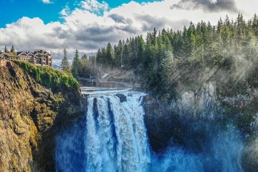A waterfall cascading down a rocky cliff, surrounded by dense forest and a lodge. 3
