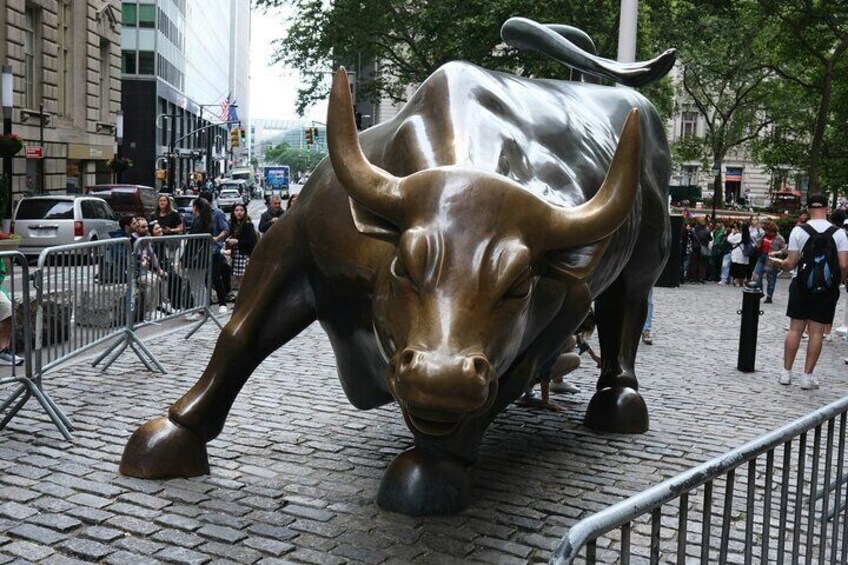 A large bronze bull statue on a cobblestone street with metal barricades and people in the background. 5