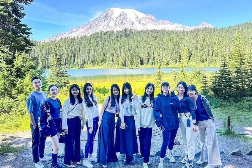 A group of people standing in front of a mountain and a lake. 1