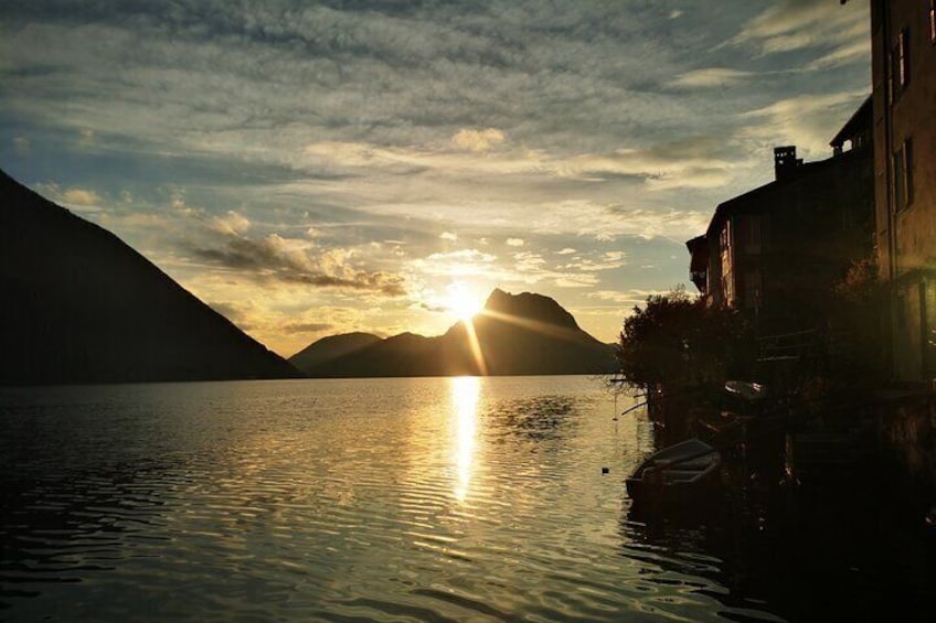 A sunset over a calm lake with mountains in the background and buildings along the shore. 3