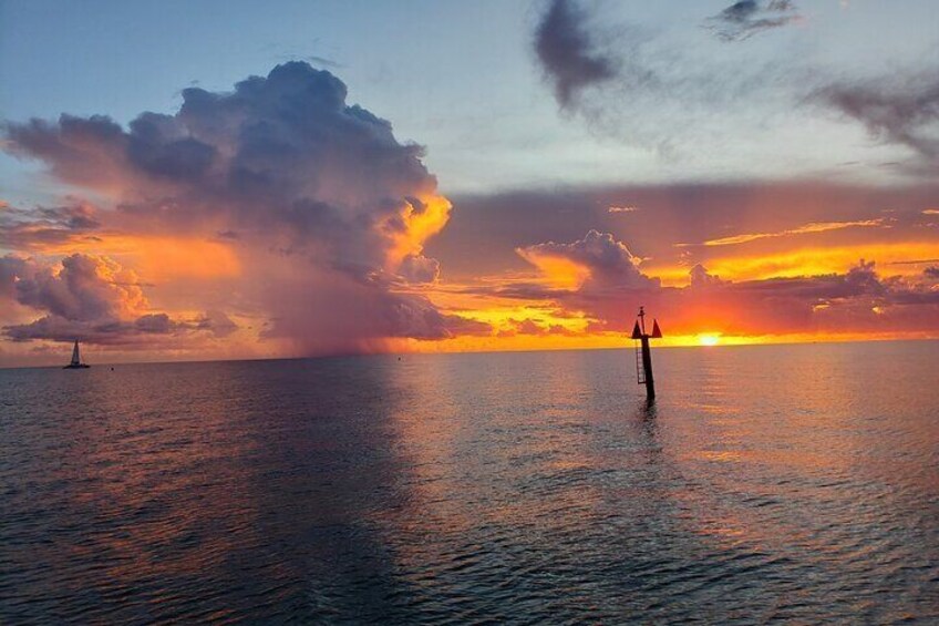 A sunset over the ocean with a sailboat and a buoy. 3