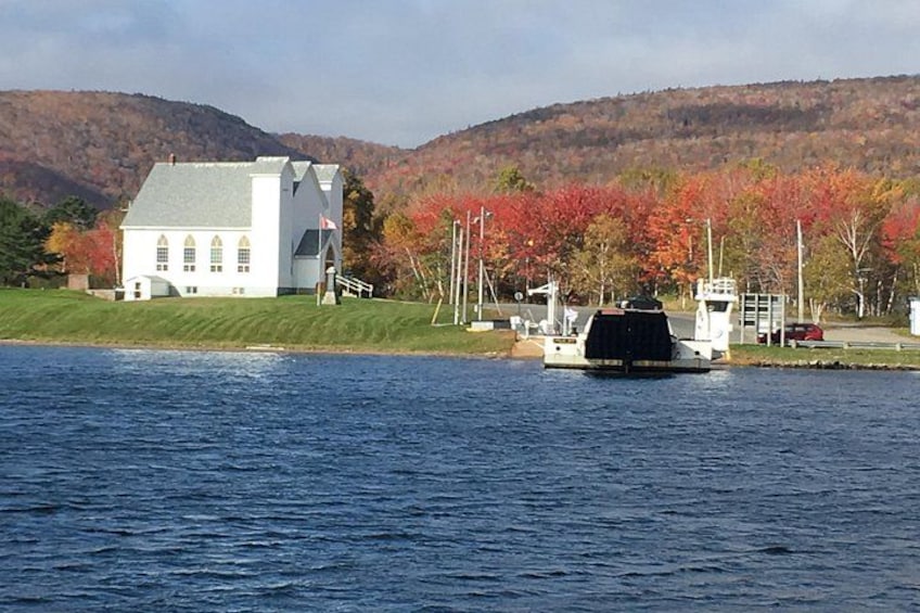 A white building with a green roof, a boat on the water, and autumn-colored trees in the background. 2