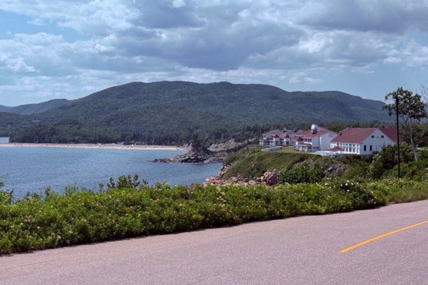 A coastal road with houses on a hillside, a body of water, and mountains in the background. 4