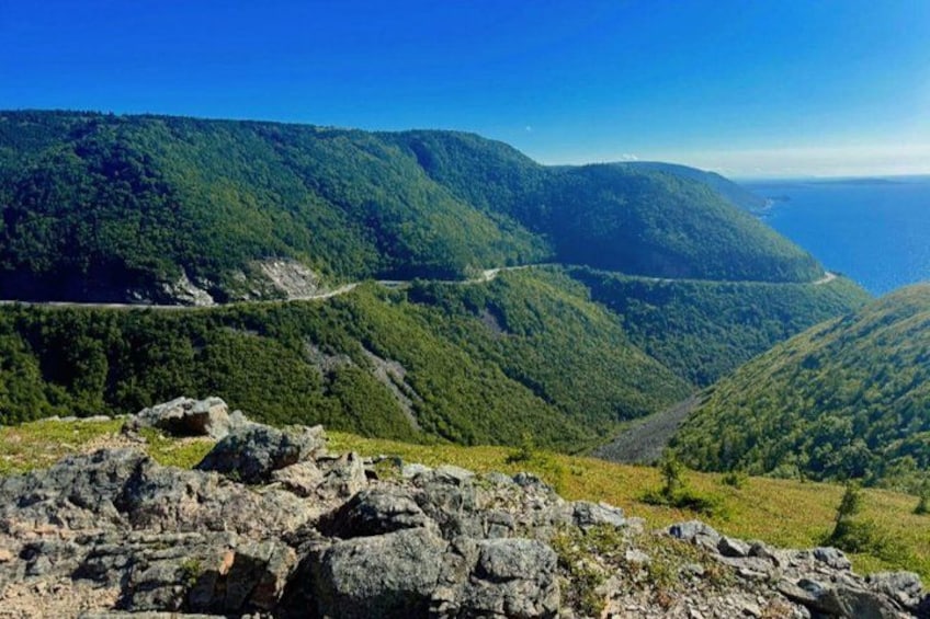 A mountainous landscape with a winding road, dense forest, and a view of the ocean. 3
