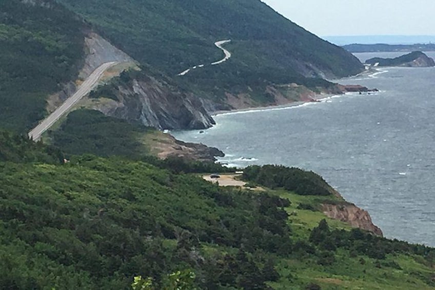 A coastal road winding through a mountainous landscape with dense greenery and a view of the ocean. 1