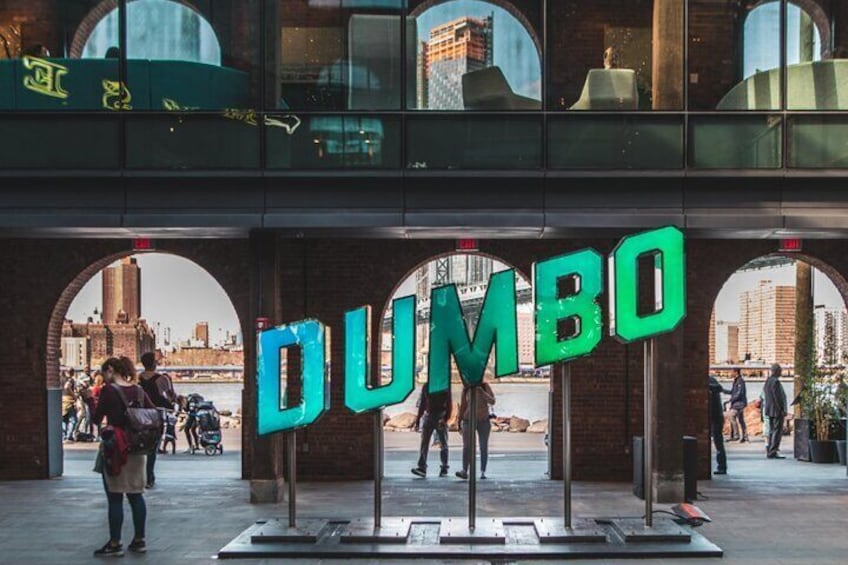 A large 'DUMBO' sign in front of a building with arched windows. 1