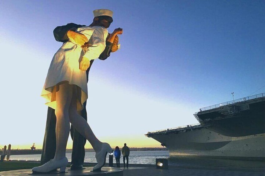 A large statue of a sailor on a pier with an aircraft carrier in the background. 5