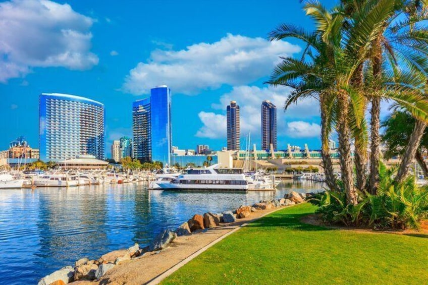 A marina with boats, a city skyline with modern buildings, and palm trees. 2