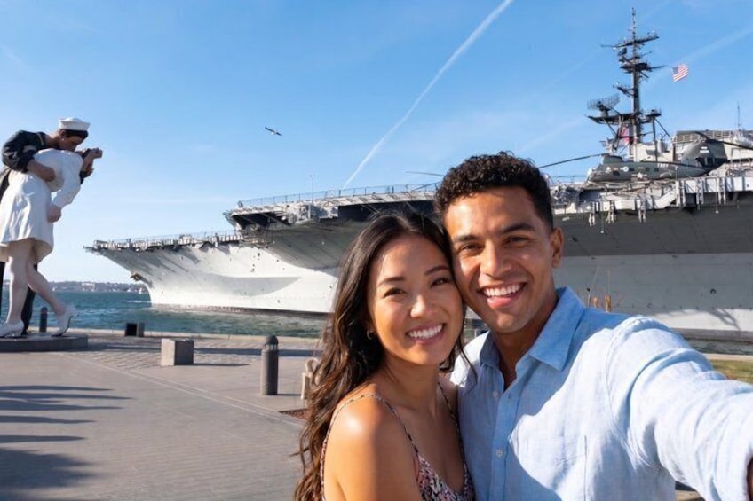 A couple taking a selfie with an aircraft carrier in the background. 4