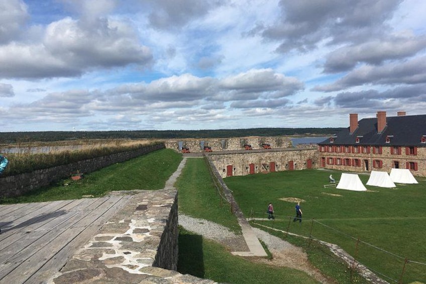 A historical fort with stone walls, a grassy courtyard, and white tents. 1