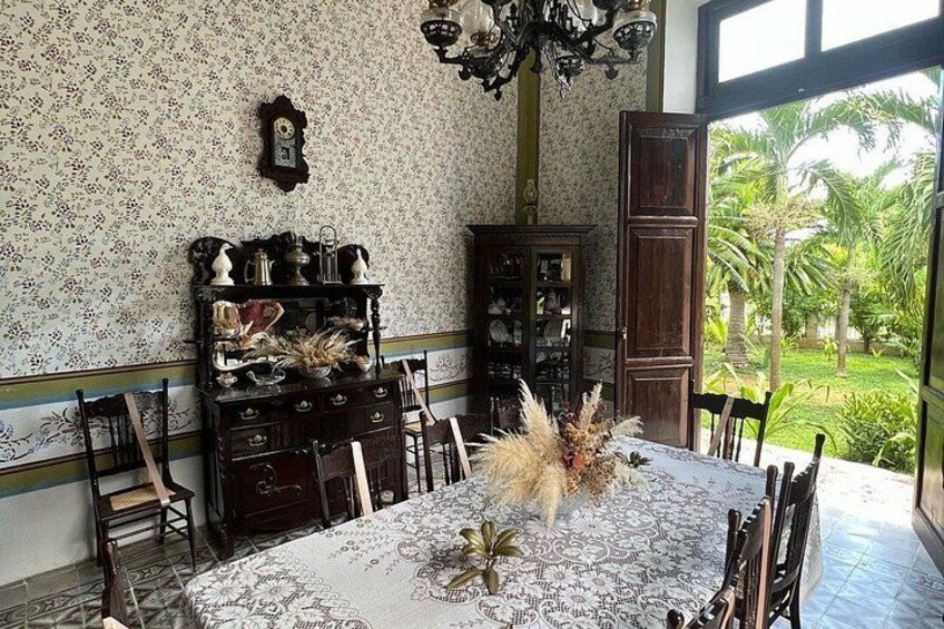A dining room with a table set for four, surrounded by chairs. There is a cabinet with various items on top and a clock on the wall. 2