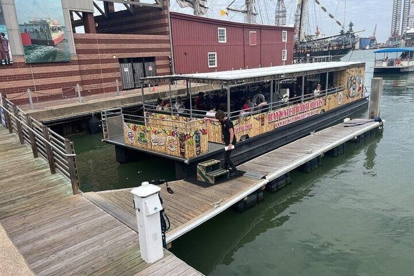 Een rivierboot aangemeerd aan een steiger met een houten looppad en een rood gebouw op de achtergrond. 4