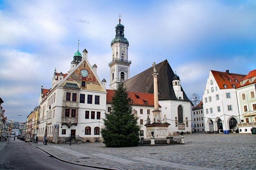 A cobblestone street with historic buildings, a church, and a Christmas tree. 3