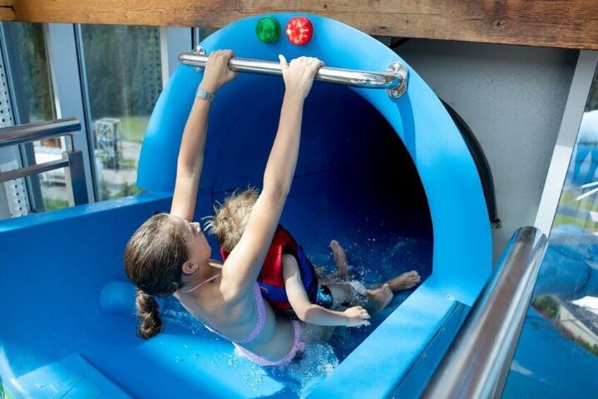 A child sliding down a blue water slide with a metal bar for support. 3