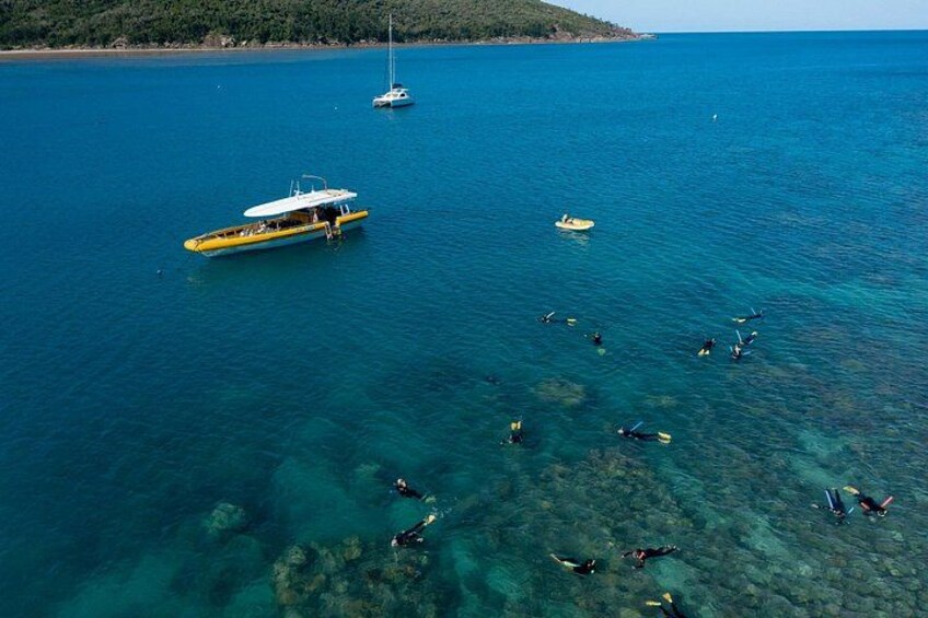 A clear blue sea with a yellow boat and several people snorkeling. 3
