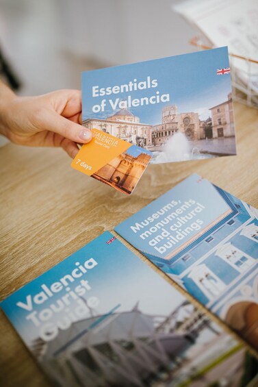 En person holder et turistkort for Valencia, med brochurer for byen på et bord. 2